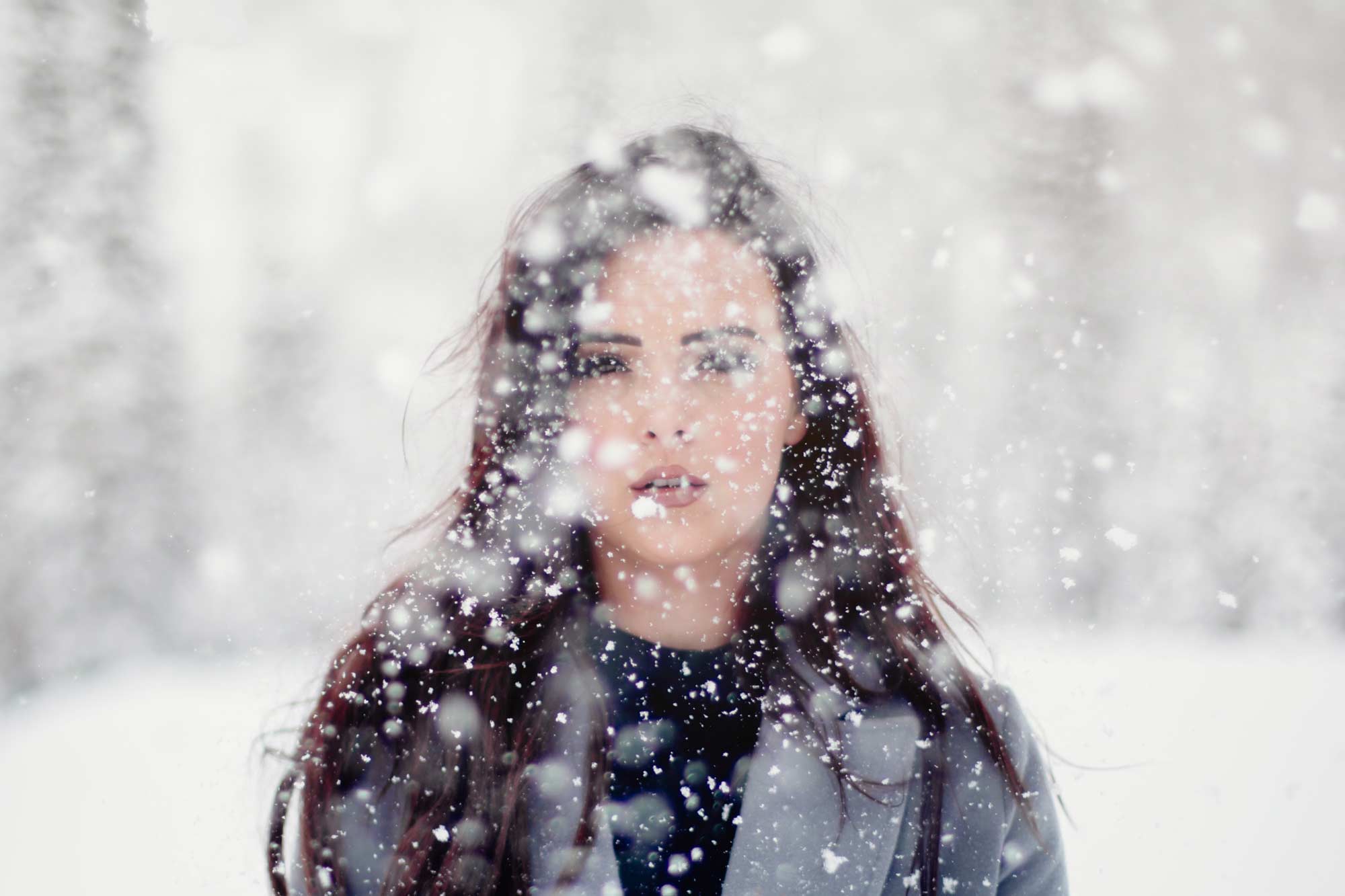 Kälte und Haut: Frau im Wald während es schneit.